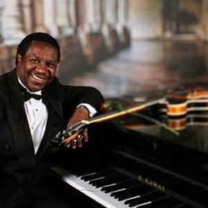 Male solo guitarist adorned in formal suit while sitting at piano with guitar sat on top for picture | Altus Entertainment